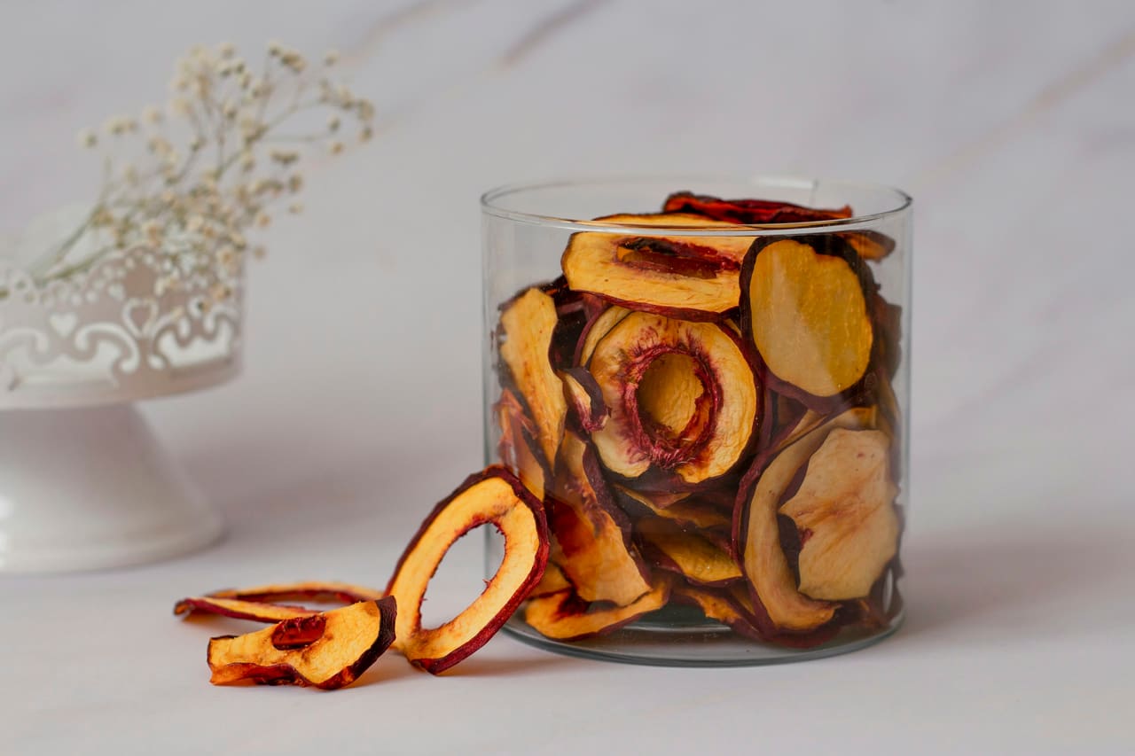 Dried apple rings in a glass jar and scattered on a marble counter